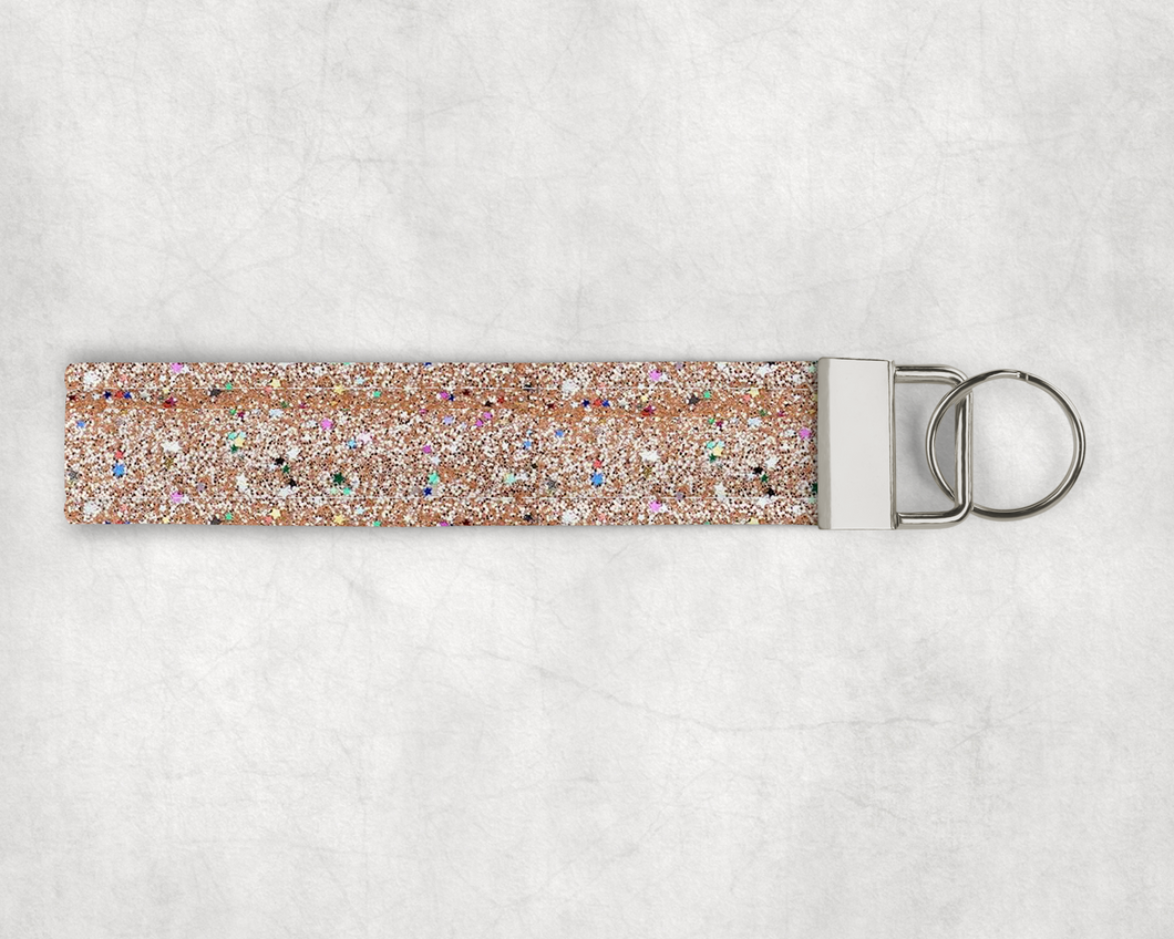 A faux leather wristlet made of a chunky glitter and star glitter fabric. The hardware cap is a metallic silver color with a keyring on the end.